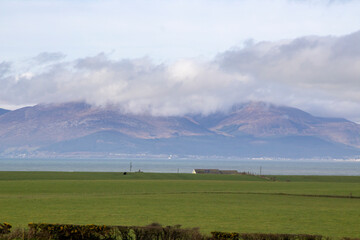 Fototapeta na wymiar 10 March 2022 A view of the Mourne Mountains with their cloud covered peaks. Viewed across Dundrum Bay from the Killough area in County Down Northern Ireland 