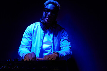 African American stylish dj creates music on a blue foggy background. Smiling dark-skinned musician...