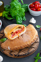 Traditional closed Italian calzone pizza with tomato sauce, mozzarella cheese and mushrooms on a board on a dark background. selective focus, copy space.