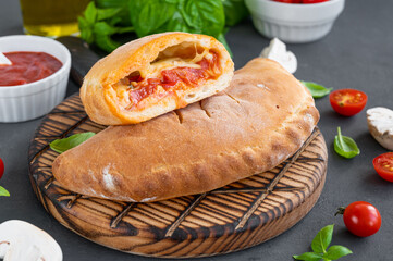 Traditional closed Italian calzone pizza with tomato sauce, mozzarella cheese and mushrooms on a board on a dark background. selective focus
