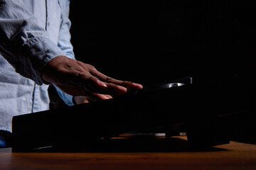 Close up of a black man's hand over a DJ console against a black background. African American man playing loud popular music in a club on professional music equipment