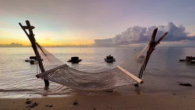 Sunset. Static shot of an empty hammock slow lying by the wind with calm waves reaching the shore from the ocean. Indian ocean. Mauritius.