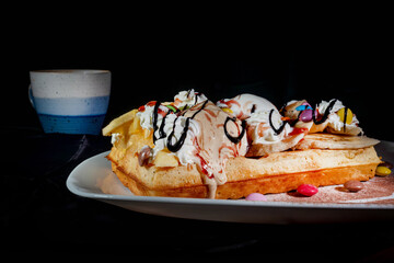 Plate of belgian waffles with ice cream, caramel sauce and fresh berries on dark background