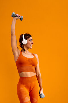 Alegre mujer deportista con unos auriculares haciendo ejercicios f&iacute;sicos sobre un fondo de color naranja