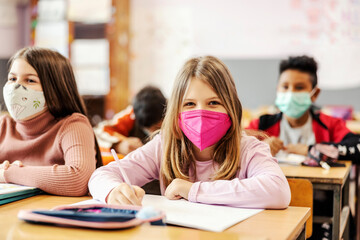 An elementary school student writing on a class with schoolmates during covid 19.
