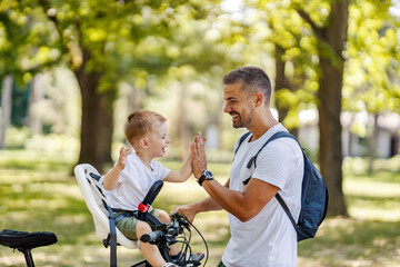 Excited father and son giving each other high five for adventure on a bike in nature.