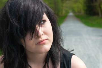 Naklejka premium Punk emo girl, young adult with black hair and eyeliner, looking away, outdoors, close-up, horizontal