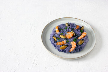 Elegant purple risotto made of red cabbage with seafood (shrimps and mussels) on gray ceramic plate, healthy food, isolated on white concrete background, copy space. Mediterranean cuisine.