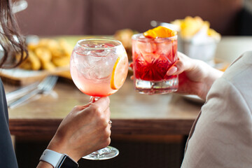 Women clinking with glasses of cocktails and sitting at the table