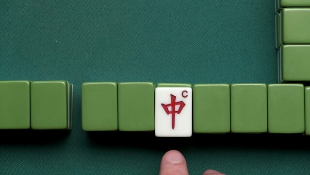 Mahjong game. Man rotate indicator of dora tile. Red dragon chun.