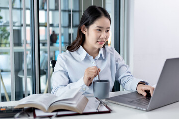 Businesswoman working on laptop and sipping coffee comfortably, Sitting in a private office, Using computers to conduct financial transactions, World of technology and internet, Work lifestyle.