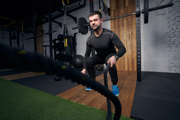 Naklejka na ściany i meble Man using fitness training battle ropes in gym