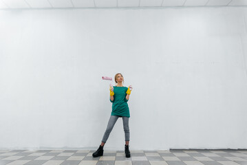 A young girl is engaged in repairs and smiles with a pink roller in her hands against a white wall in a new apartment. Renovation of the interior and a new apartment. 