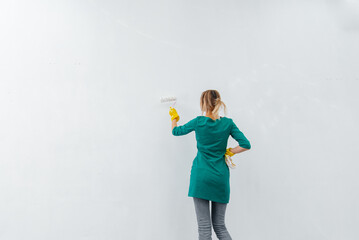 A young girl is engaged in repairs and smiles with a pink roller in her hands against a white wall in a new apartment. Renovation of the interior and a new apartment. 