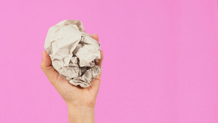Crumpled paper. It is mauled in a woman's hand on pink backgroud. top view.