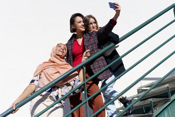 Cheerful multiracial women taking selfie on smartphone on stairs