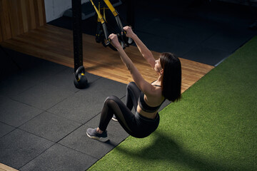 Sporty woman using hanging training straps in gym