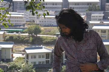 Fototapeta na wymiar A long haired and bearded young guy posing outdoor with college campus in background with copy space 