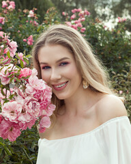 Fototapeta premium charming smiling beautiful young blonde woman in rose flowers garden