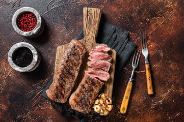 Grilled Lamb sirloin fillet meat on wooden board with herbs, mutton loin steak. Dark background....