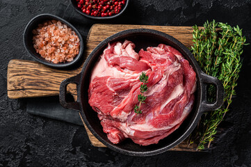 Boneless lamb neck, raw meat in a skillet with herbs. Black background. Top view