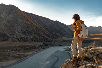 Girl hiker with backpack stands in mountains near river