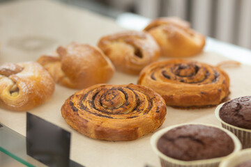 Variety baked muffins and buns in glass showcase at bakery cafe.