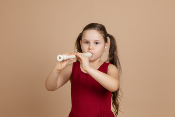 Girl in red dress thoughtfully play melody on flute, blowing air into duct, beige background. Learn...