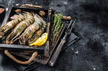 Raw fresh Giant Black tiger prawns shrimps in a tray with lemon and thyme. Black background. Top...