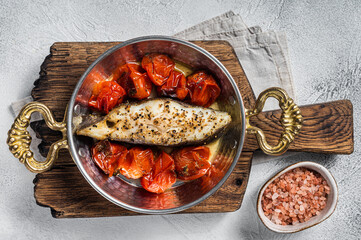 Fried halibut fish steaks with tomato in skillet. White background. Top view