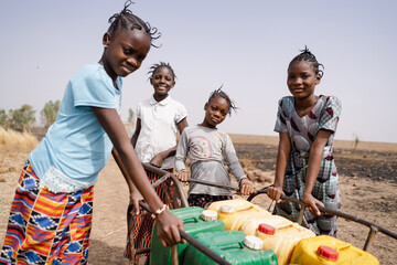 Four pretty African girls pushing a cart full of heavy water cans together; symbolic for union is...