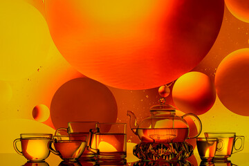 transparent glass teapot and cups with tea and drops on colorful background 