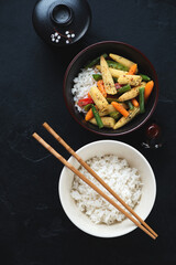 Bowls with stir-fried vegetables and white rice, top view on a black stone background, vertical shot