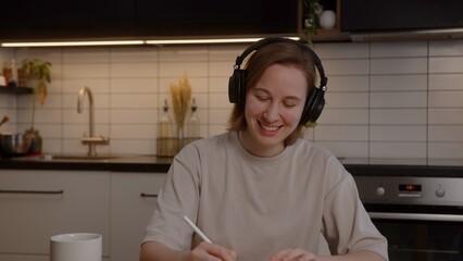 Beautiful girl in headphones listens to music, rejoices and uses a laptop in the living room