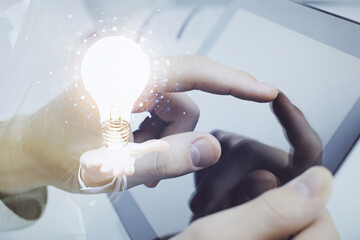 Double exposure of man's hands holding and using a digital device and bulb hologram drawing. Idea concept.