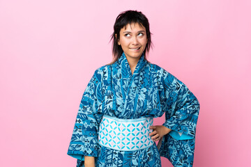 Young woman wearing kimono over isolated blue background having doubts while looking up
