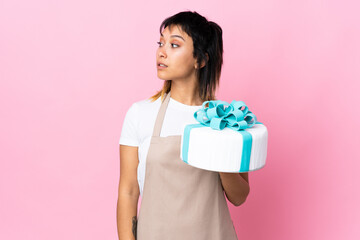 Uruguayan Pastry chef holding a big cake over isolated pink background looking side