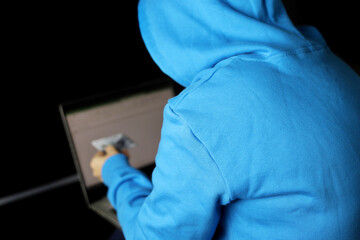 Cybercrime and hacking bank accounts. Unrecognizable hacker in blue hoodie sitting with laptop and credit card in hand