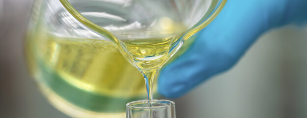 Scientist hand wearing glove pouring petroleum yellow lubricating oil high viscosity into test tube in the laboratory. Automotive and industrial oil technology concept