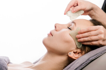 Obraz na płótnie Canvas Gua sha massage of a woman in a beauty salon over white background.