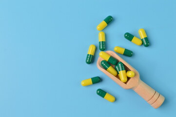 Wooden scoop and pill capsules isolated on a blue background. Copy space for the text.