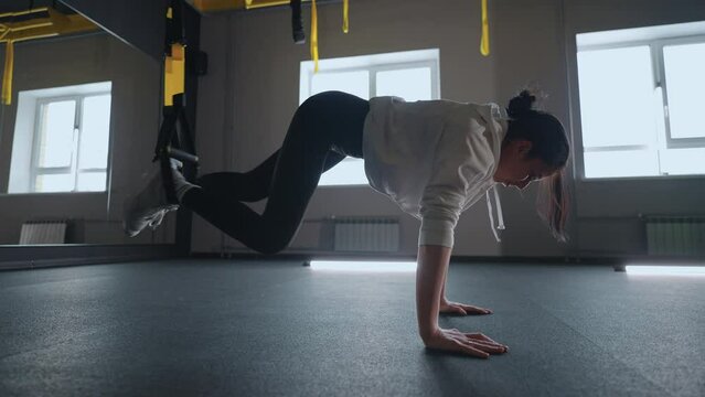 Doing TRX exercises. Young athletic woman in sports clothing training legs with trx fitness straps in the gym. exercise where stabilizing muscles trained and the whole body is working truly functional