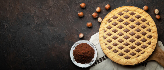 Tart with hazelnuts and cocoa powder on wooden cutting board. Top view on brown plaster background,...