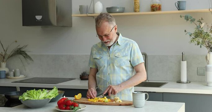 Fresh, natural food delivery services, healthy lifestyle, family recipe concept. Senior man in glasses cutting paprika, prepare vegetarian salad, makes homemade meal, dietary lunch caring about heath