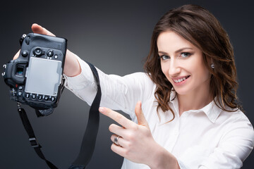 Pretty girl photographer holds a professional camera in her hands and points a finger at a digital monitor
