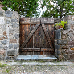 A natural wood door and low stonewall fence with trees and potted plants, Pachia Rahi village, Aegina island, Greece