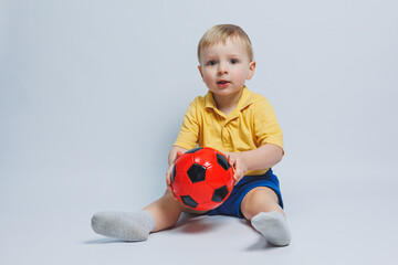 Little european boy, fan or player in yellow and blue uniform with a soccer ball, supports the soccer team on a white background. Football sport game, lifestyle concept. Isolated on white background