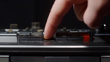 A finger presses the rewind button on an old shiny cassette recorder - close-up