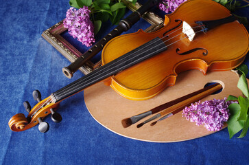 Fototapeta premium Flowers in vases, violin, art palette and brushes on a table with a blue tablecloth.