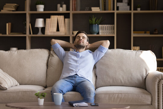 Peaceful Millennial Guy Relax At Quiet Cozy Living Room Dream Enjoy Tranquility Peace Of Mind. Calm Mindful Young Man Take Break From Work Study Recline On Sofa In Comfortable Pose Keep Eyes Closed